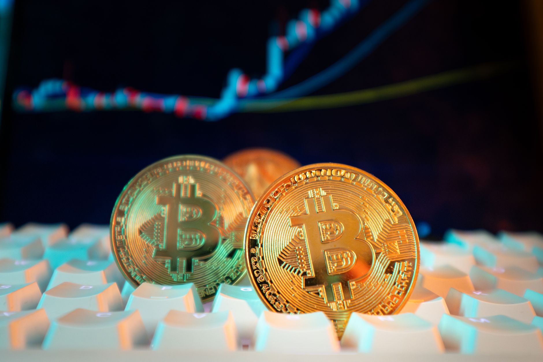 Ilustrasi: Golden Bitcoin coins on a keyboard with a financial chart in the background, representing digital currency and market trends.