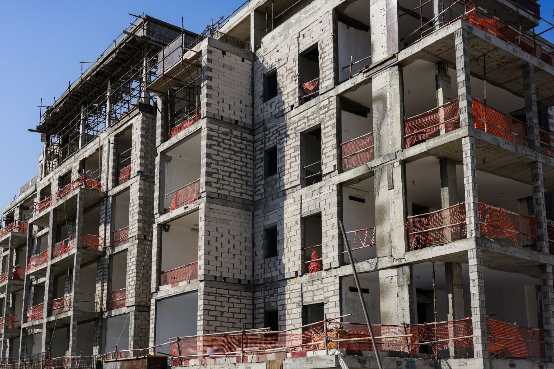 Ilustrasi: A modern multi-story apartment building under construction with scaffolding and safety netting.