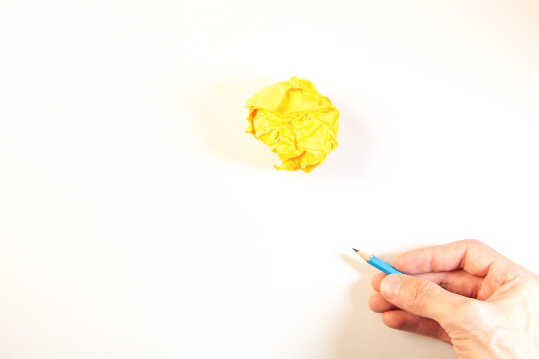 Ilustrasi: Hand holding pencil near crumpled yellow paper ball