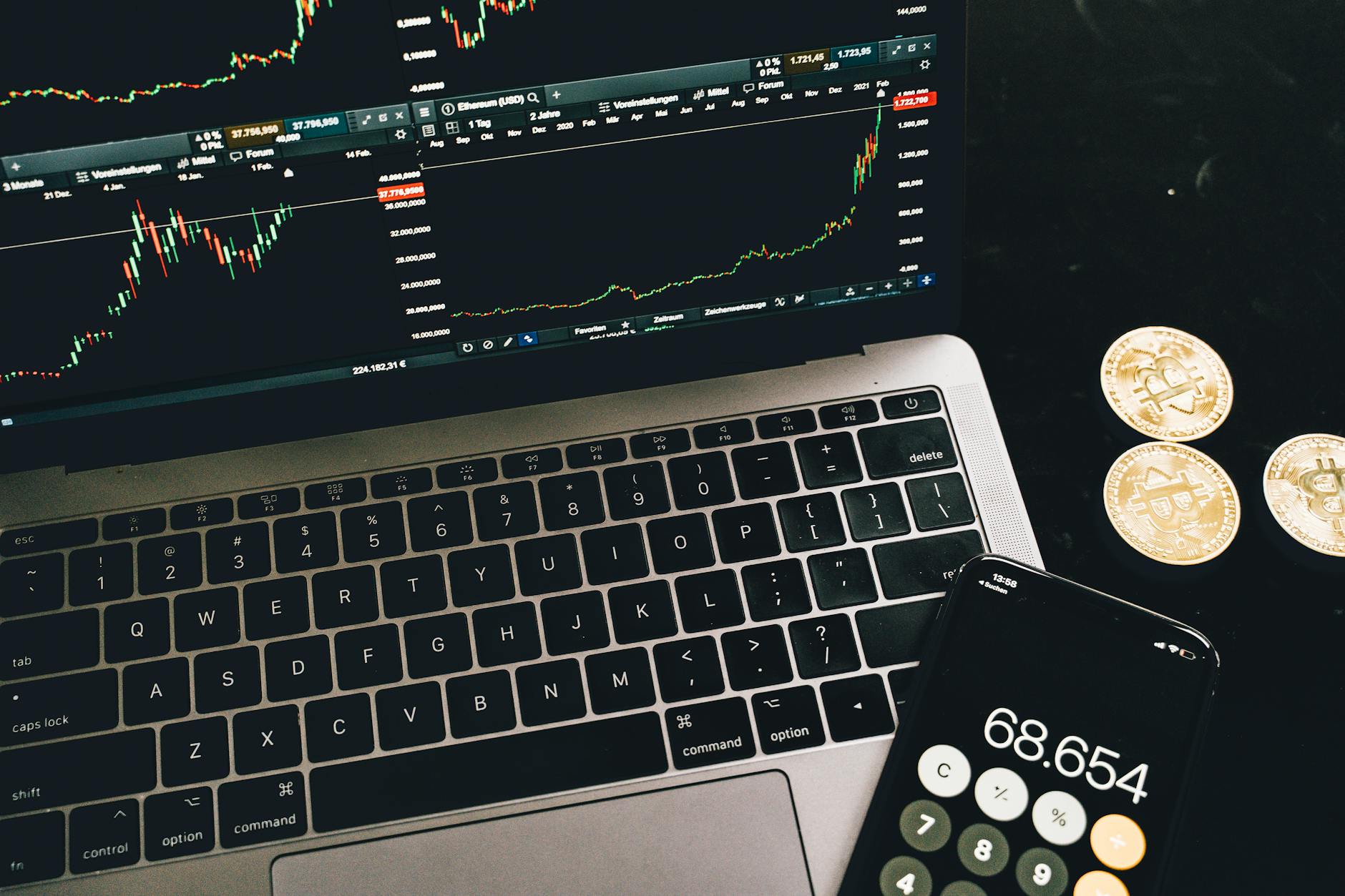 Ilustrasi: A laptop with trading charts, smartphone calculator, and bitcoin coins depicting cryptocurrency trading.