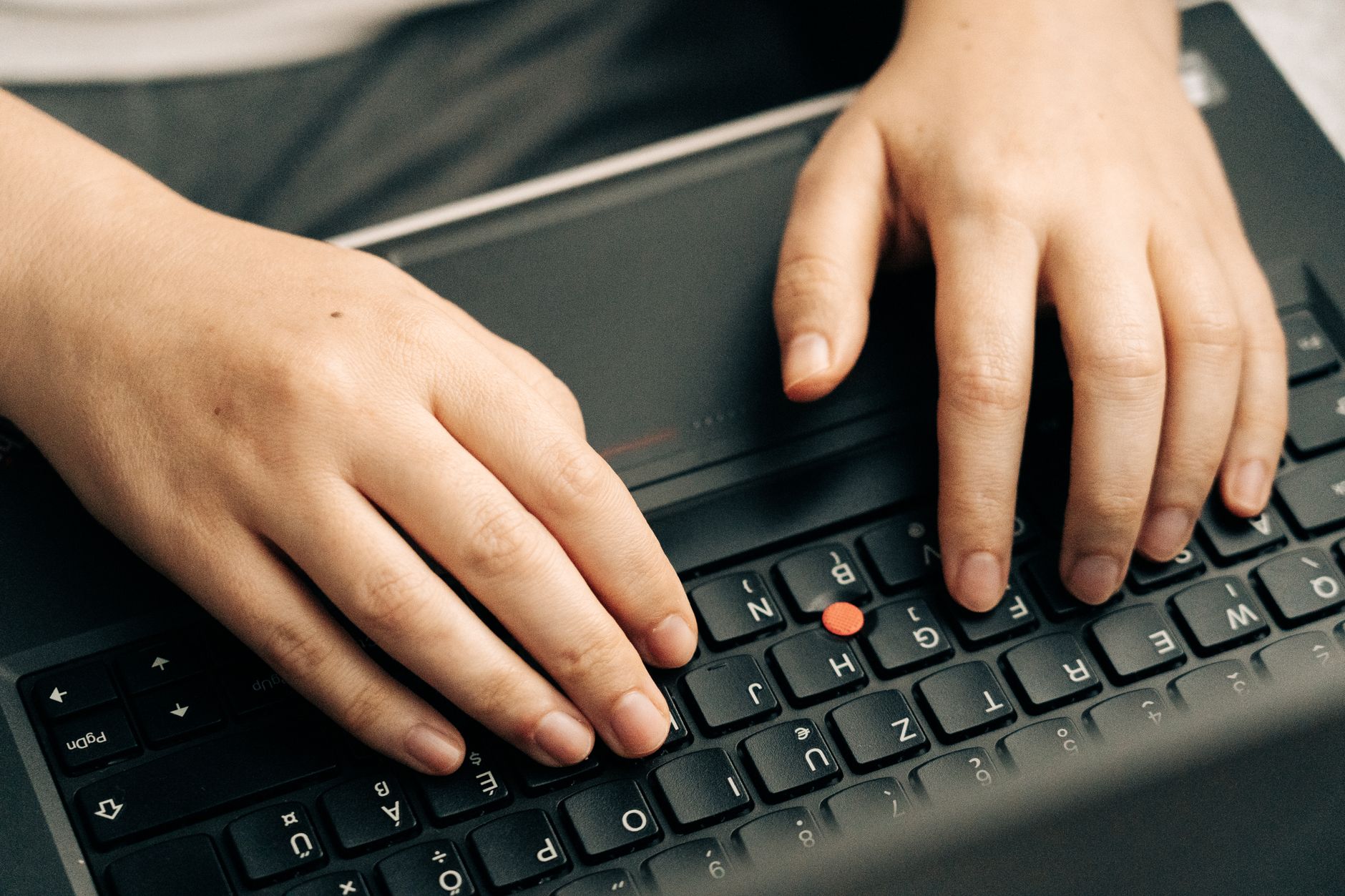 Ilustrasi: Close-up of hands typing on a black laptop's keyboard emphasizing productivity.