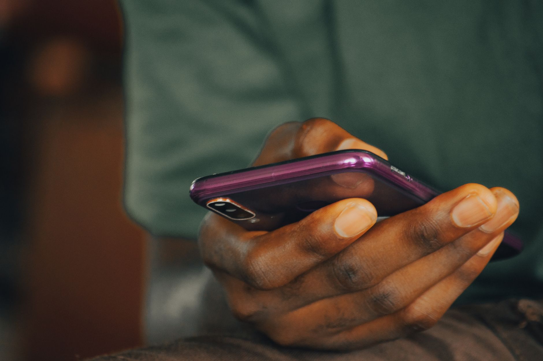 Ilustrasi: A close-up shot of a person holding a purple smartphone indoors, focusing on texting or browsing.