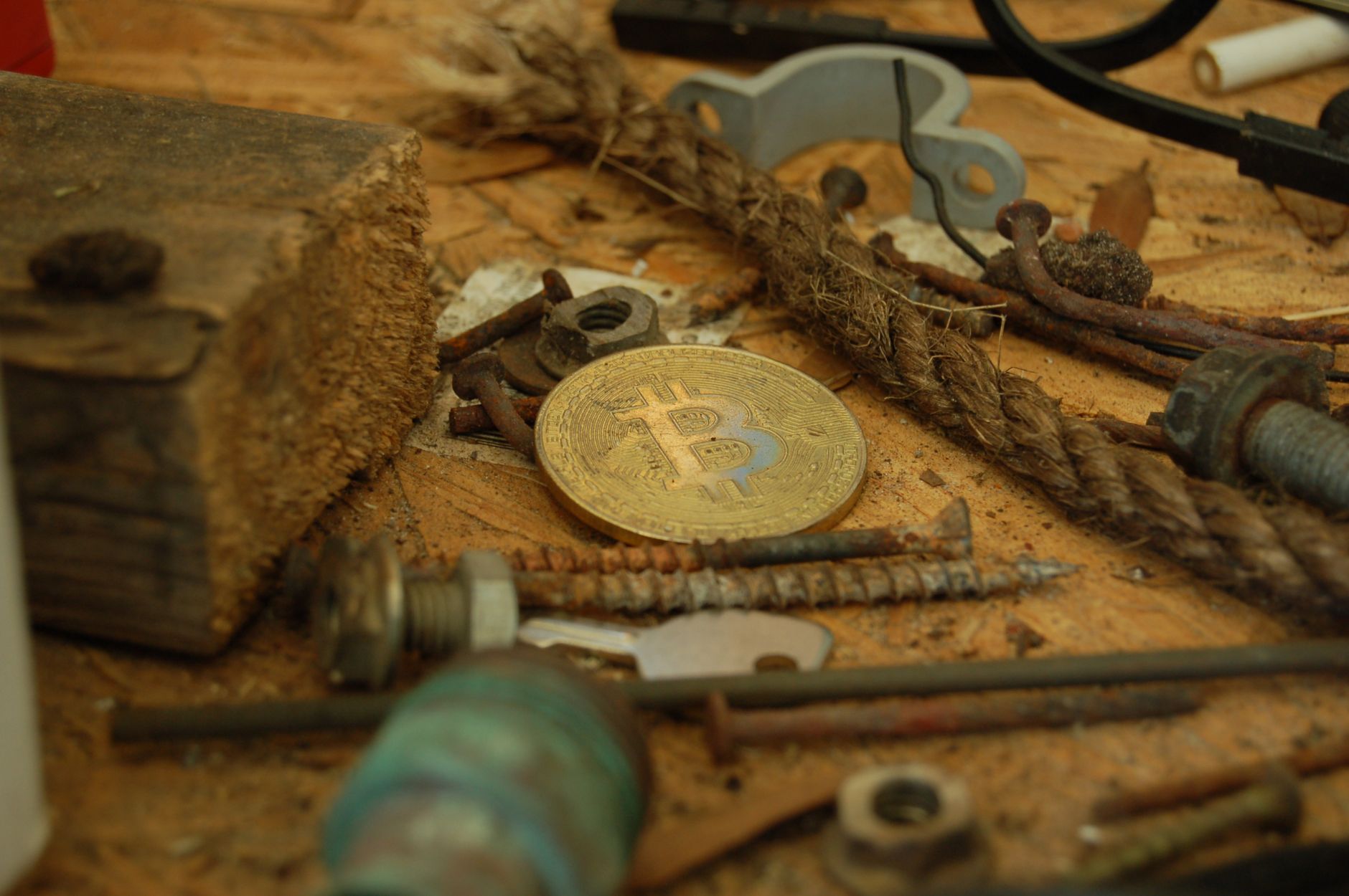Ilustrasi: A bitcoin coin placed among various tools and hardware pieces on a wooden surface.