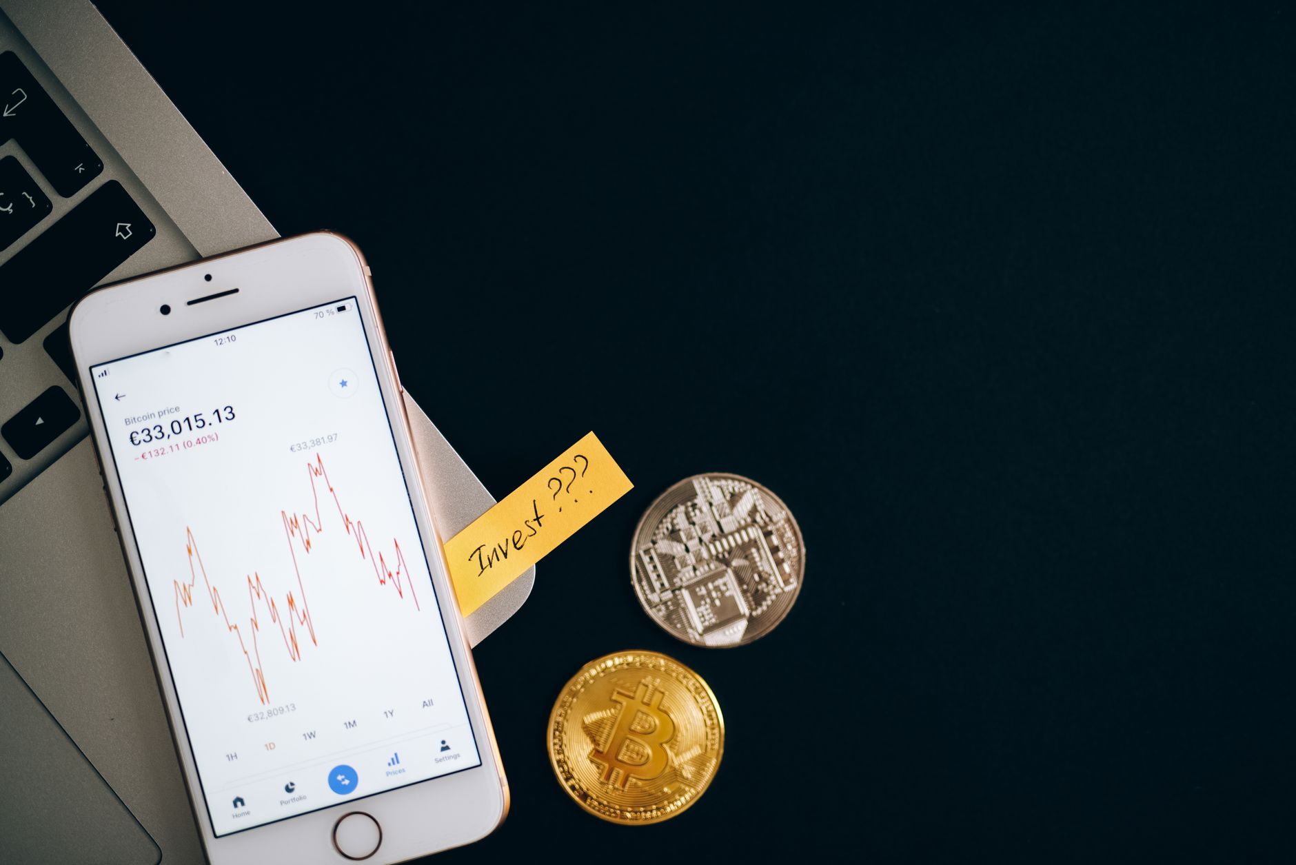 Ilustrasi: A smartphone displaying cryptocurrency prices beside coins and a laptop, symbolizing investment.