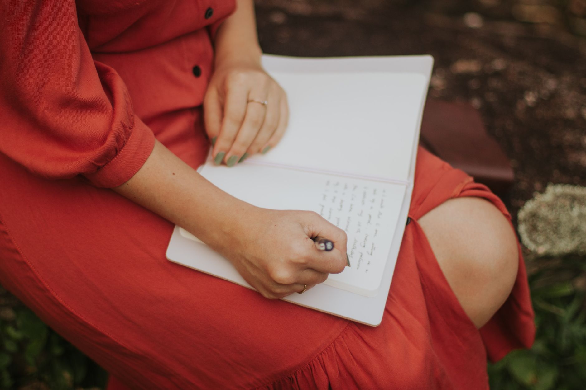 Ilustrasi: A woman in a red dress writing in a journal, outdoors over a leafy background.