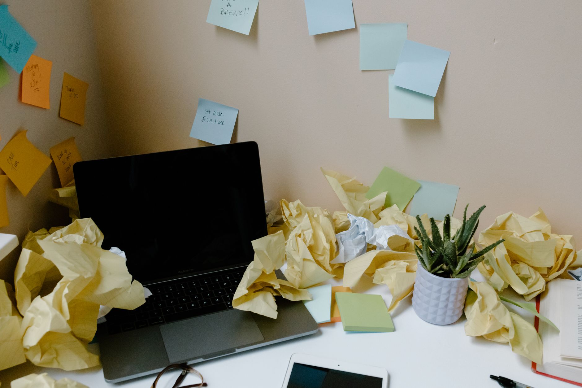 Ilustrasi: A chaotic office desk with a laptop, scattered papers, sticky notes, and a potted plant.