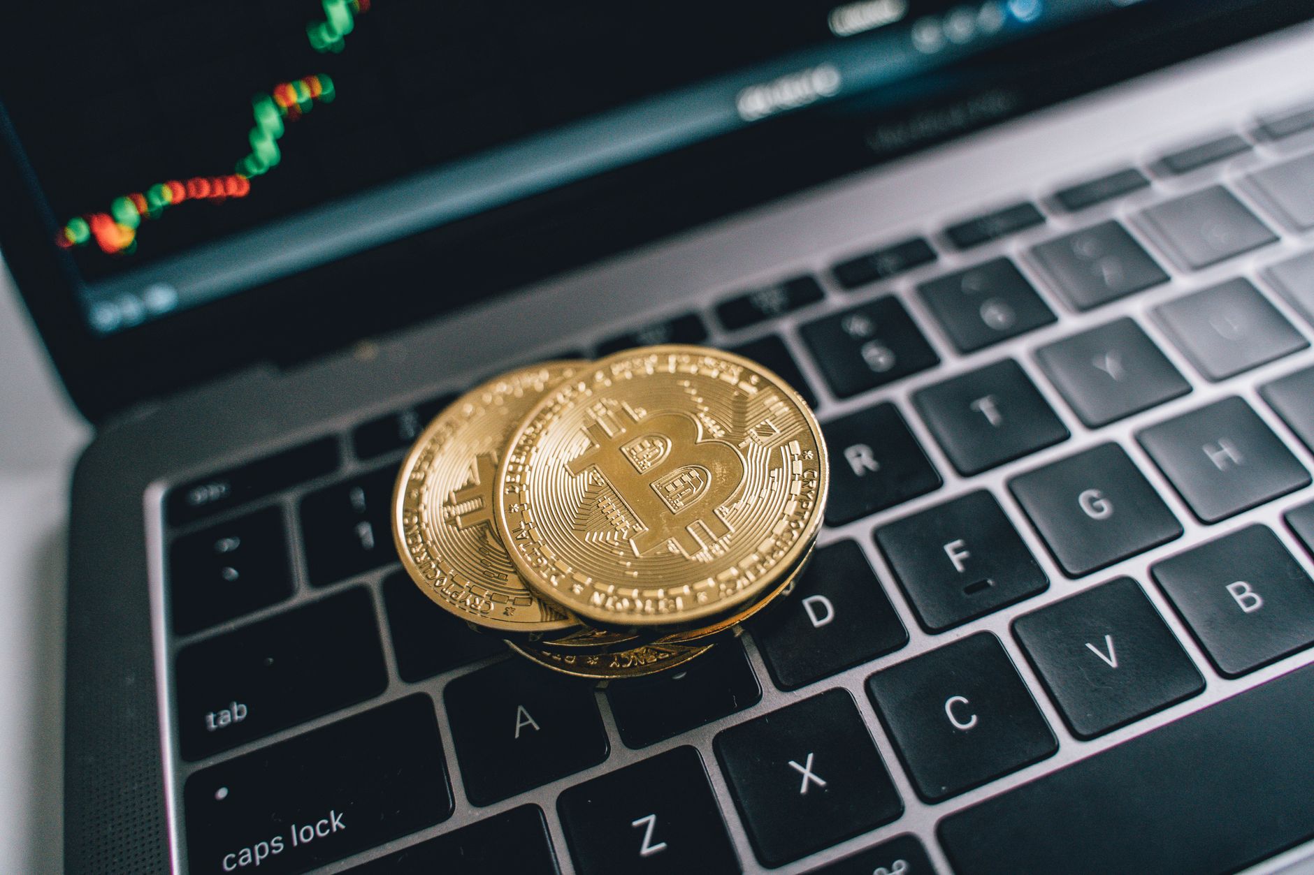 Ilustrasi: Close-up of golden bitcoins on a laptop keyboard depicting cryptocurrency and trade concepts with a market chart in the background.