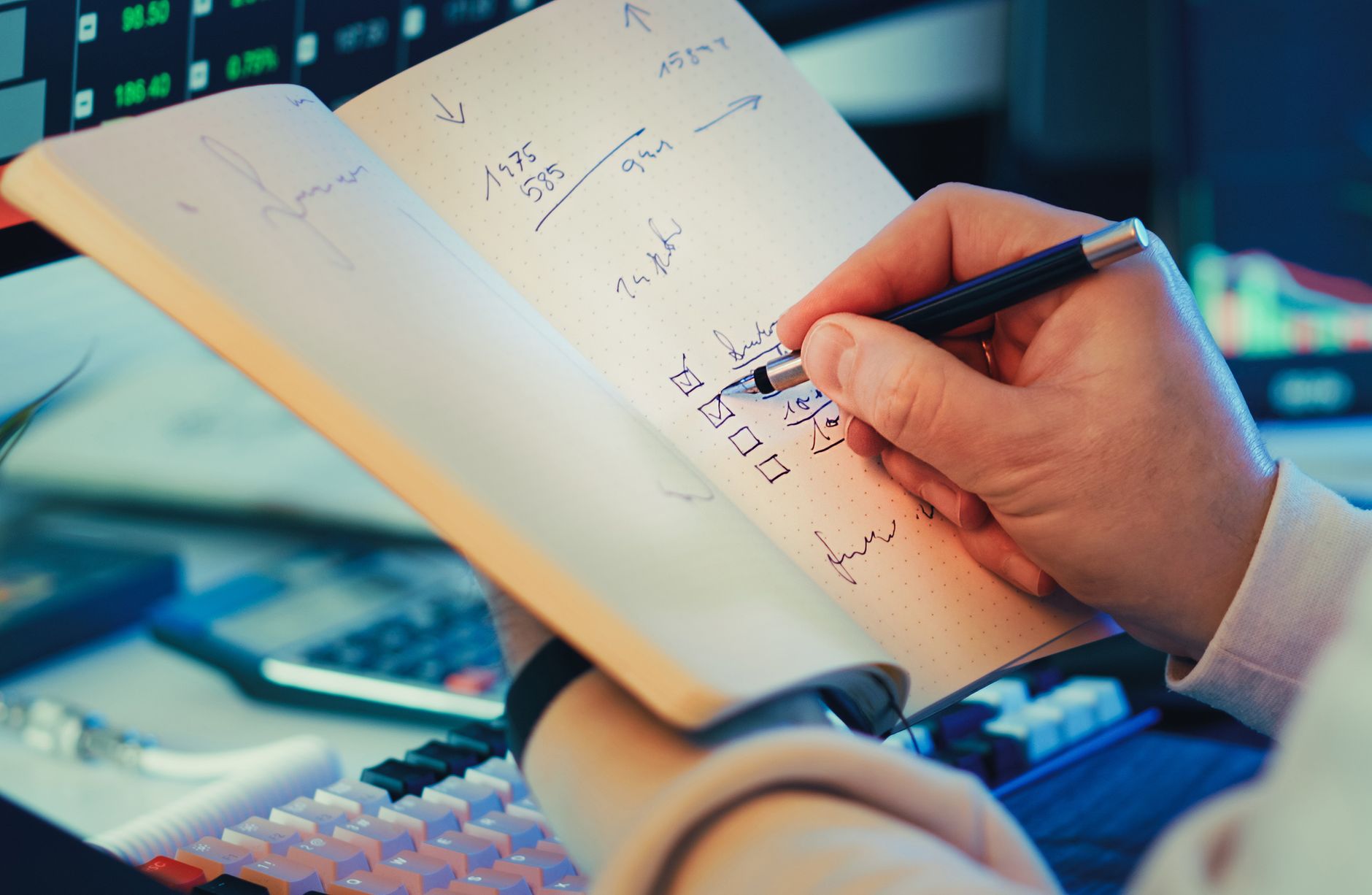 Ilustrasi: A hand writing in a notebook during stock market analysis on a desk.