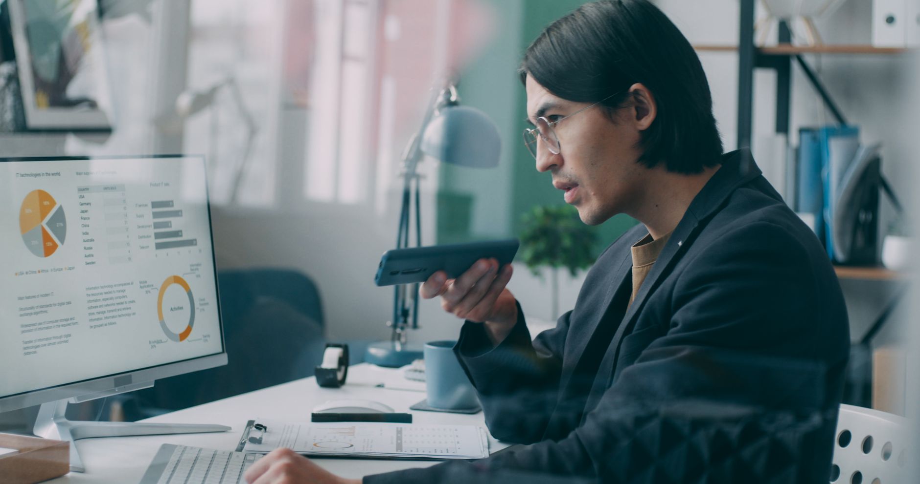 Ilustrasi: Business professional analyzing data charts on a computer while speaking on phone in an office setting.
