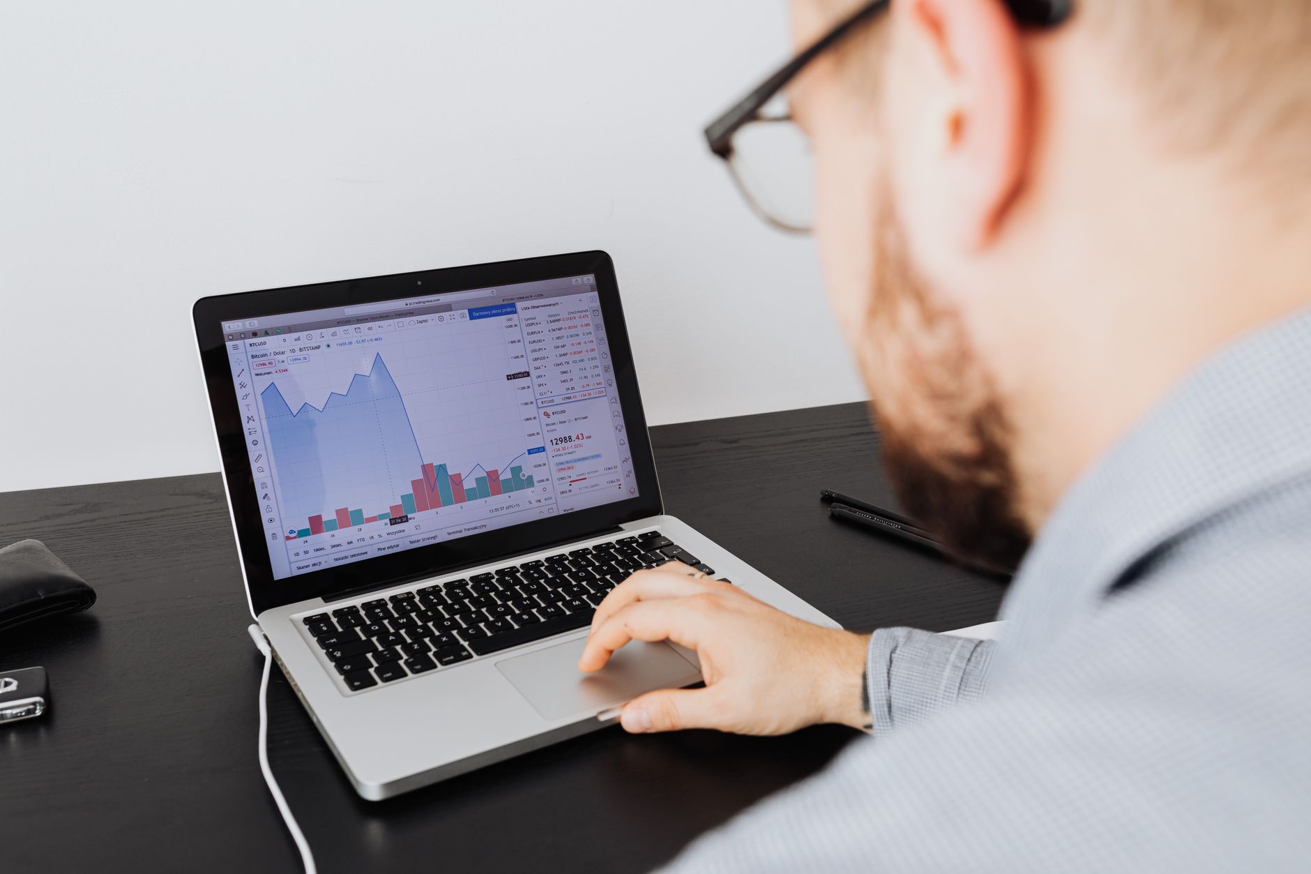 Ilustrasi: Man working on a laptop analyzing business data and financial graphs indoors.