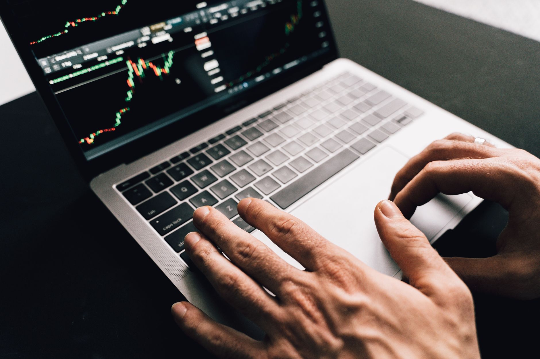 Ilustrasi: Close-up of hands typing on a laptop with stock market graphs, ideal for finance or business themes.