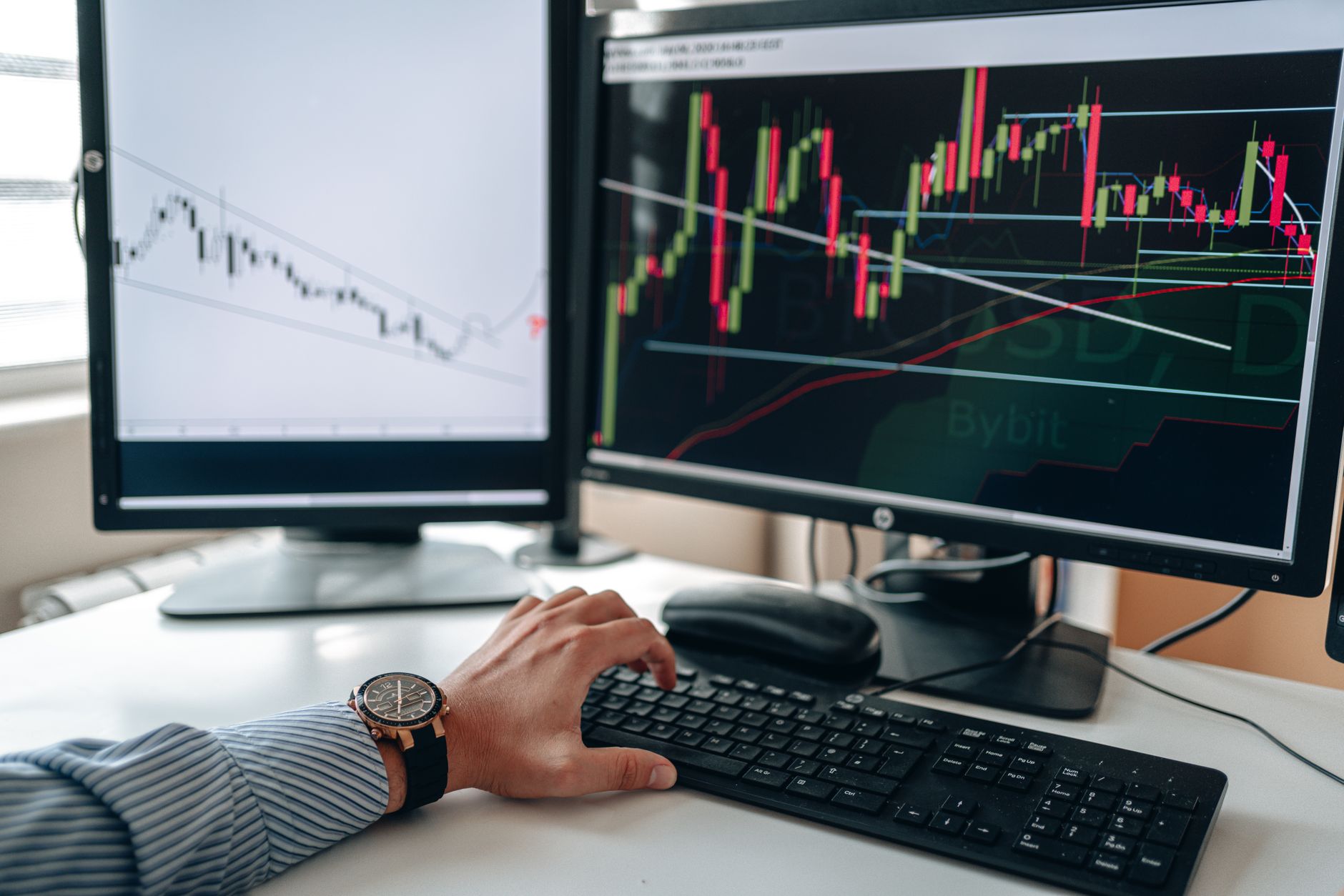 Ilustrasi: A businessperson using dual monitors to analyze stock market trends with charts and graphs.