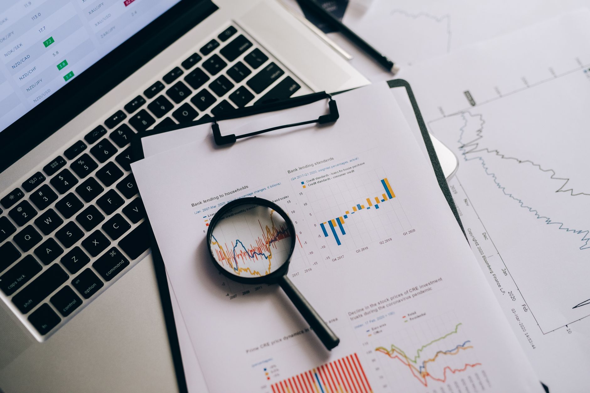 Ilustrasi: Overhead view of financial charts, laptop, and magnifying glass, ideal for business analysis themes.