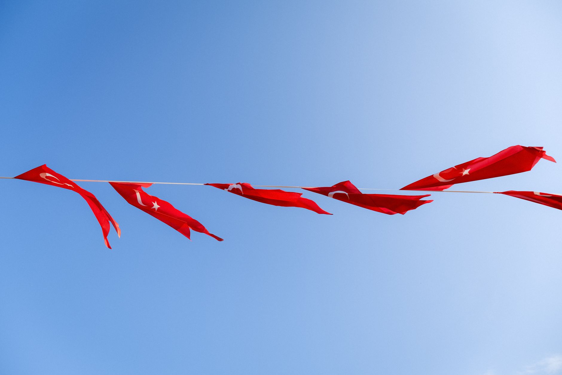 Ilustrasi: Red Turkish flags flutter on a line against a clear blue sky, symbolizing national pride and freedom.