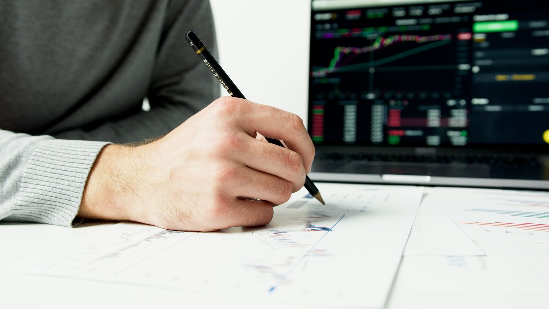Ilustrasi: Close-up of a person analyzing financial charts with a laptop displaying stock market data.