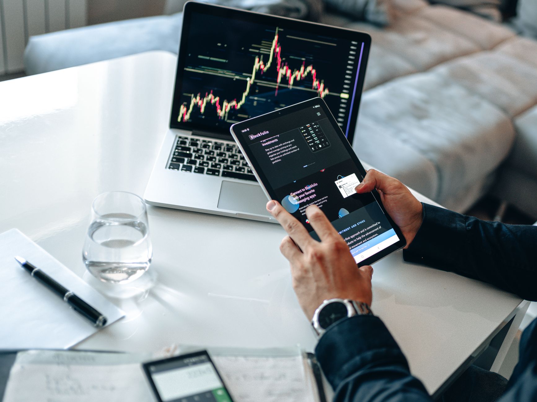 Ilustrasi: Person analyzing digital market trends on tablet with laptop showing financial charts.