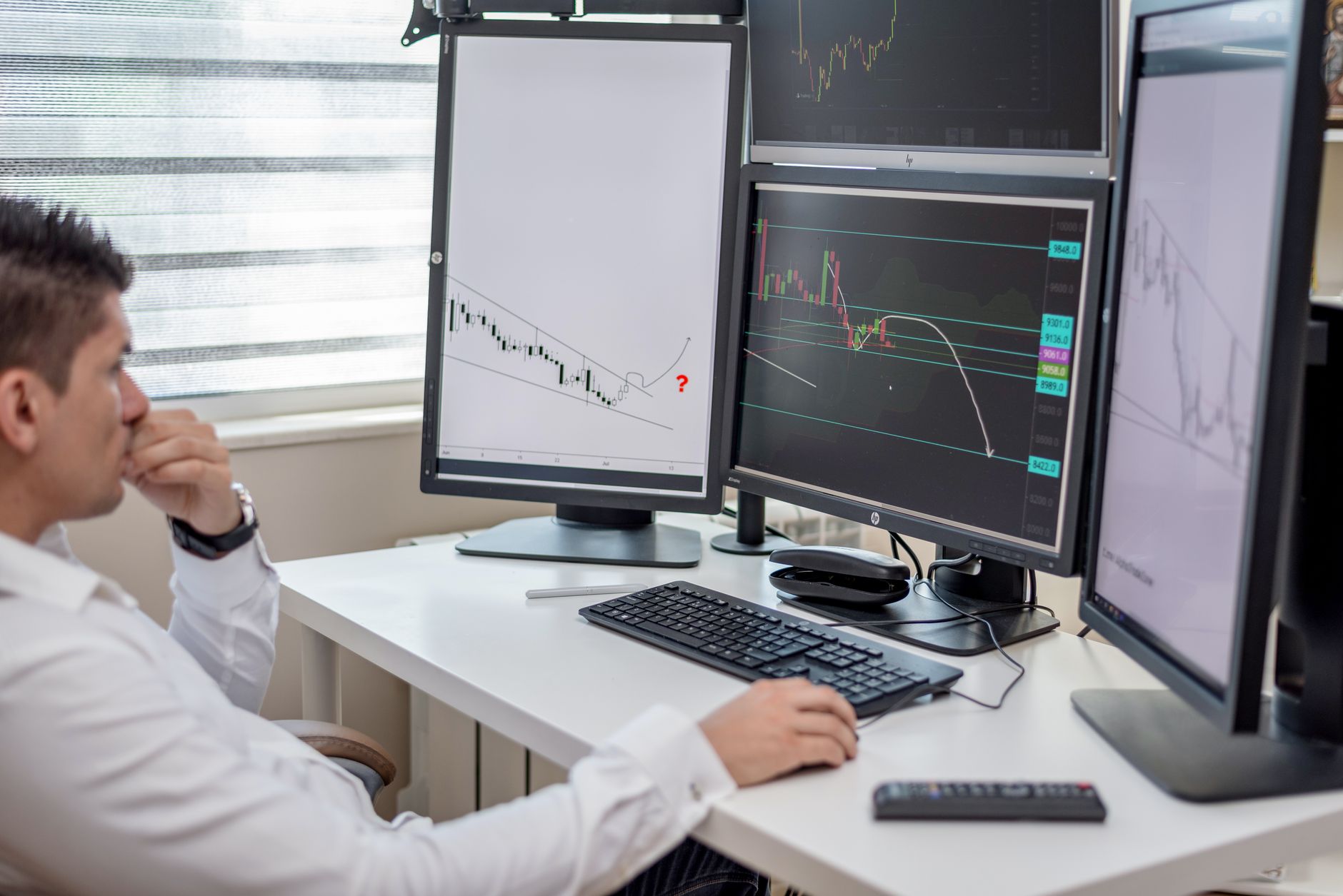 Ilustrasi: Business professional analyzing financial data on multiple computer monitors at his workspace.