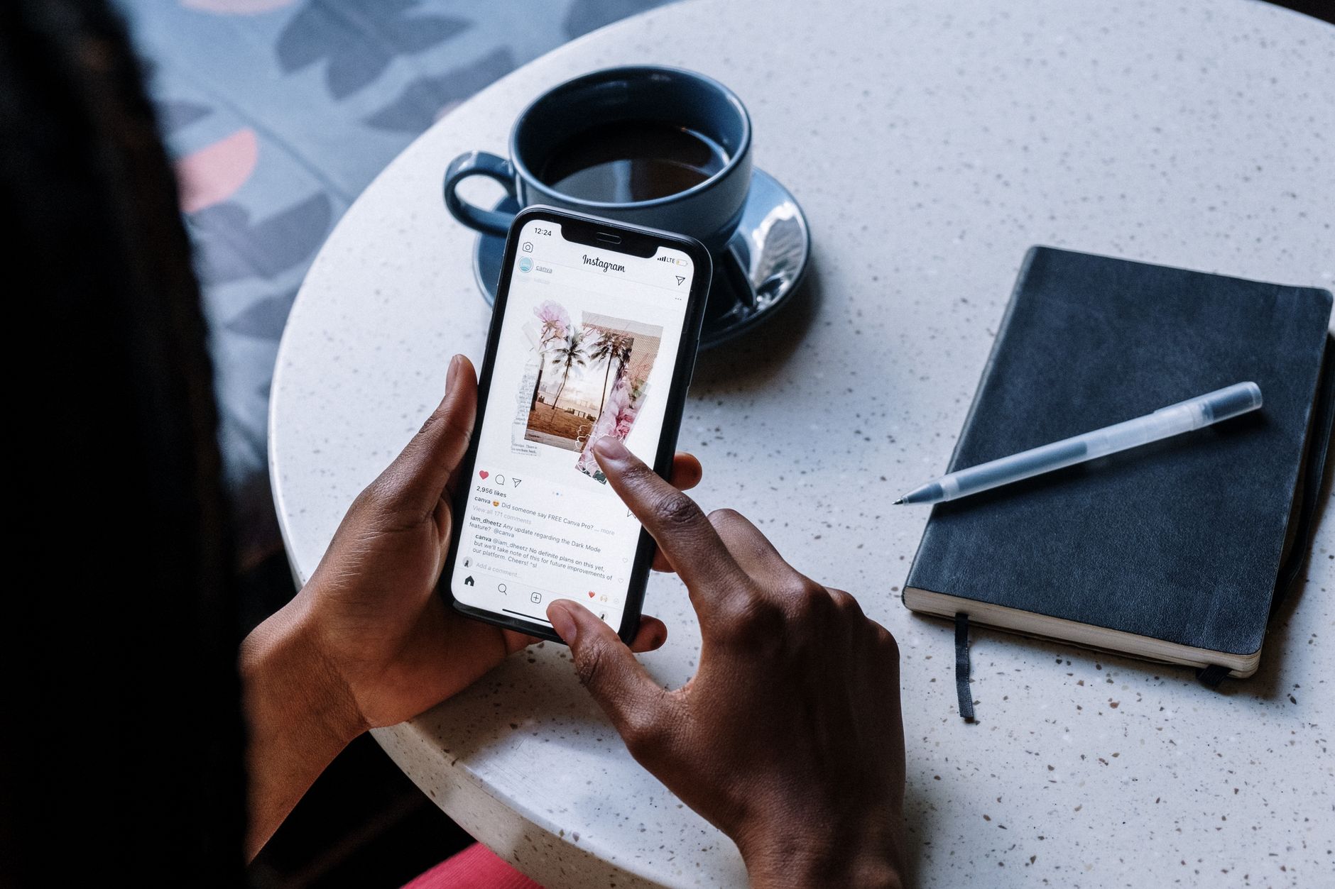 Ilustrasi: Hands holding smartphone at a cafe table with coffee and a notebook, focusing on social media browsing.