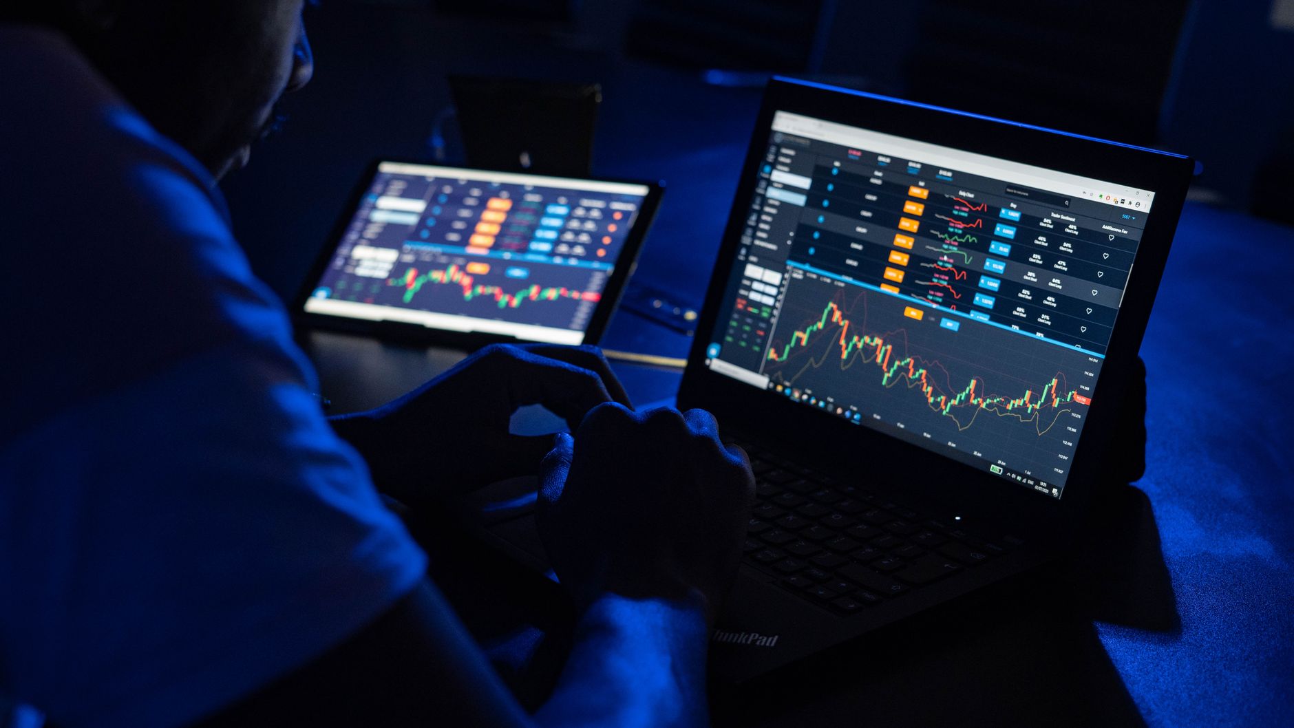 Ilustrasi: Man analyzing financial charts and data on laptops in a dimly lit room, highlighting forex trading.