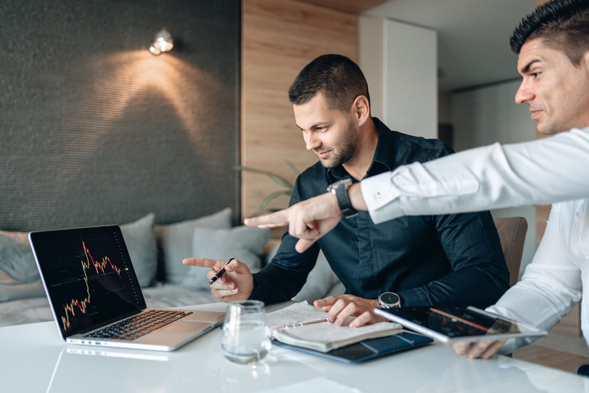 Ilustrasi: Two businessmen reviewing financial data on a laptop indoors, analyzing market trends.